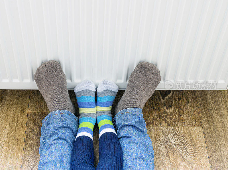 一个男人和一个小孩穿着冬天的袜子，在加热器附近暖脚。