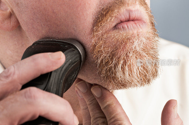 男人用电动剃须刀小心地修剪圆胡子