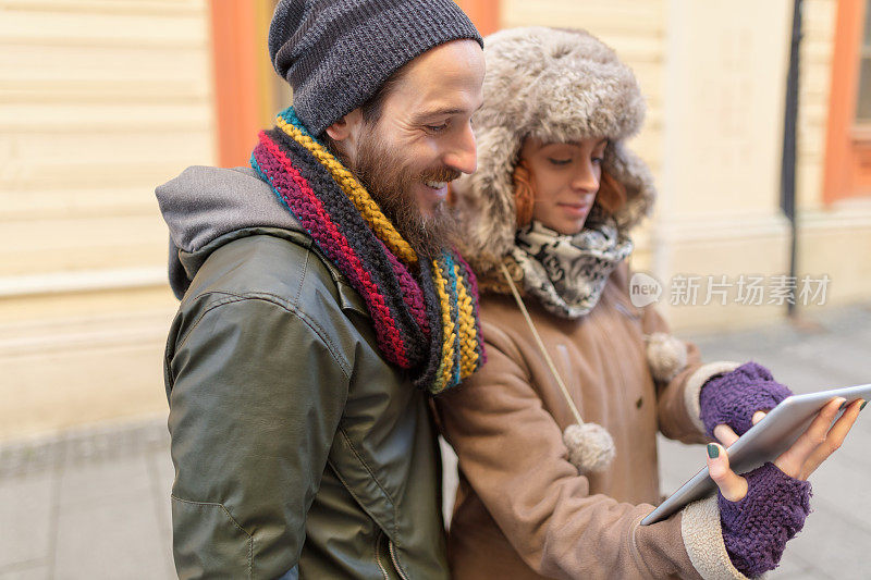 戴着冬季帽子的年轻夫妇在平板电脑上浏览街道指示
