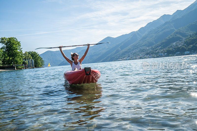 在山上的湖上，红色的独木舟上，欢快的女人举起双臂