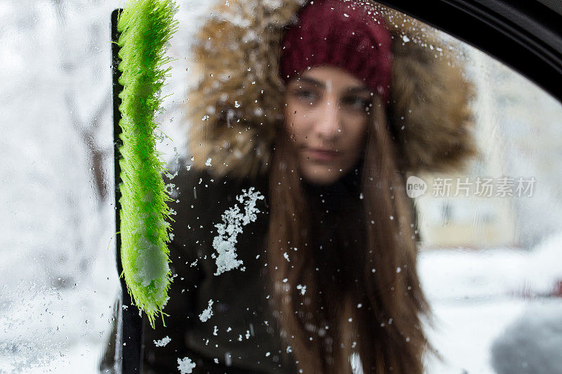 年轻女子正在清理车窗上的雪