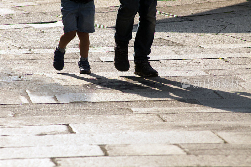 孩子们的腿在石头铺成的街道上背光的细节。
