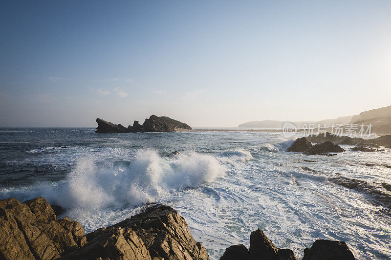 傍晚时分，海浪拍打着布满岩石的海岸线，撞击着天空