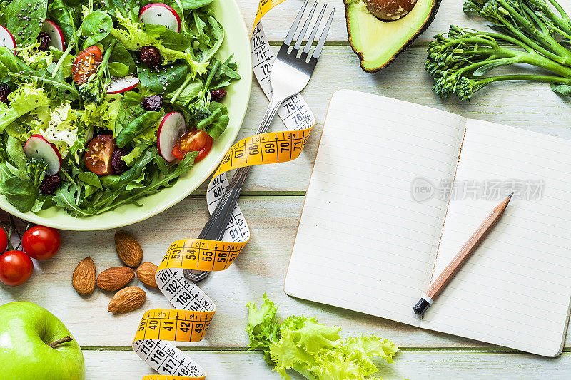 健康饮食和节食的概念:新鲜健康的沙拉，水果，卷尺和一个空白的记事本