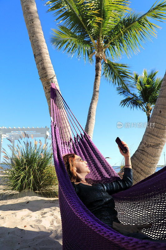 美丽的女人自拍和放松在热带沙滩上的吊床