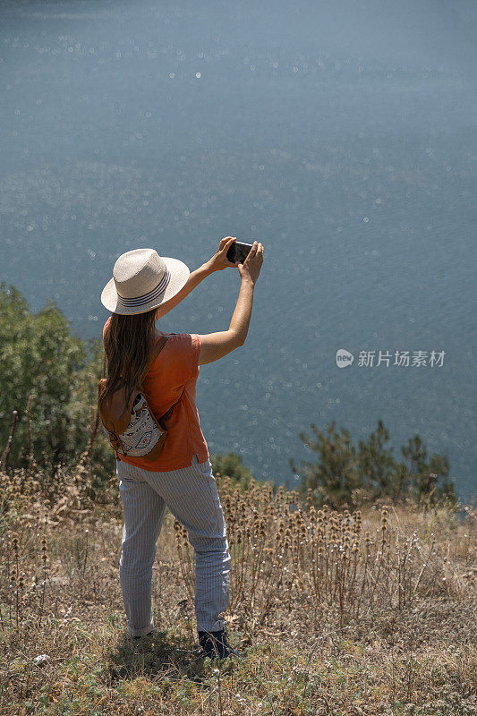 回归自然。一个人用智能手机拍照。一个快乐的年轻女游客漫步在大自然中。阳光明媚的户外享受。