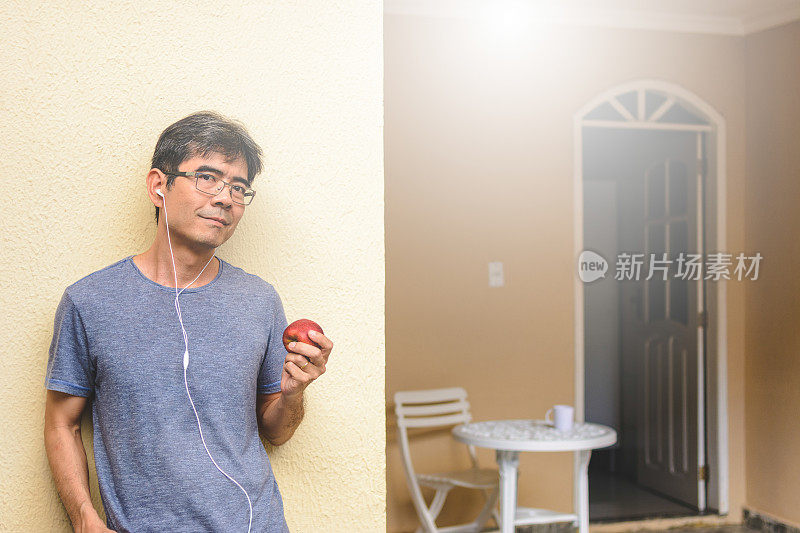 成熟的亚洲男人戴着耳机，拿着苹果。健康饮食的概念