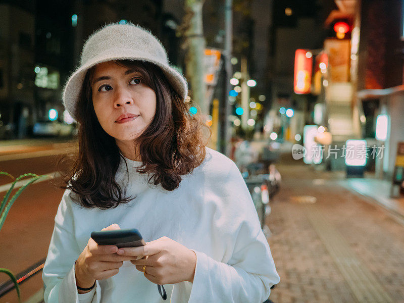 年轻女子晚上用智能手机享受城市生活