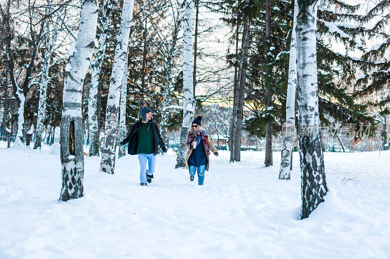 一对快乐的年轻夫妇在公园的雪地上奔跑