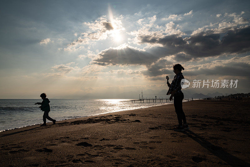 年轻女子用智能手机在海滩上拍摄男孩