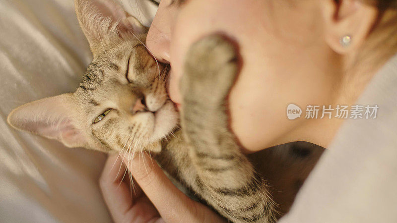 一个年轻女子在卧室白色的床上亲吻她的宠物猫。