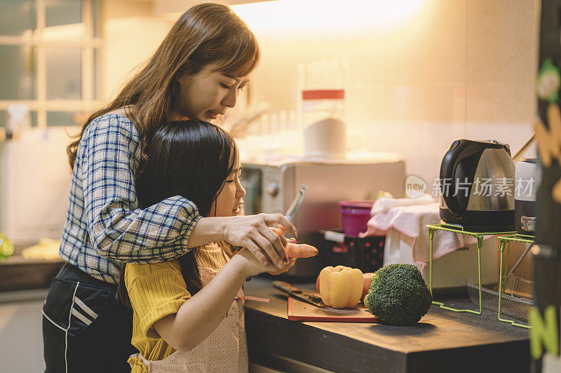一位亚洲华人母亲在厨房里准备食物，她和女儿在一起切菜