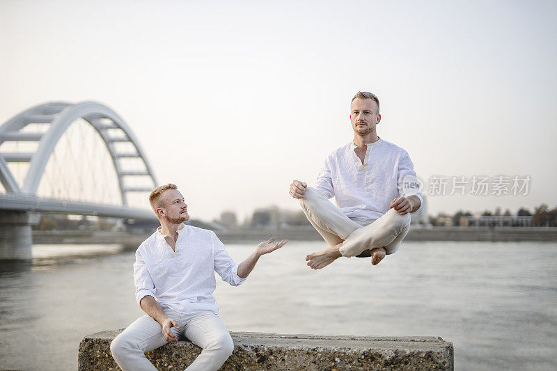 年轻美丽的男子在半空中沉思的肖像，漂浮在户外地面上，坐在莲花姿势，莲花身