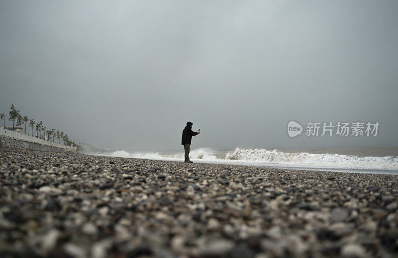 土耳其安塔利亚，下雨天，一名身穿黄色雨衣的男子在海滩上拍照
