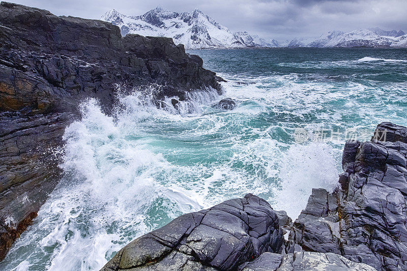 咆哮的海洋附近的岩石海岸风景如画的罗浮敦群岛与雪山在挪威的春天。水平的形象