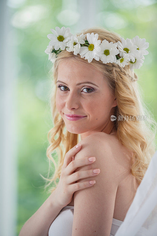 美丽的新娘戴着花冠，从肩上看着镜头，微笑着