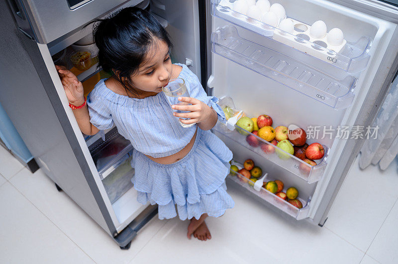 可爱的小女孩在冰箱附近拿着装满淡水的水杯。
