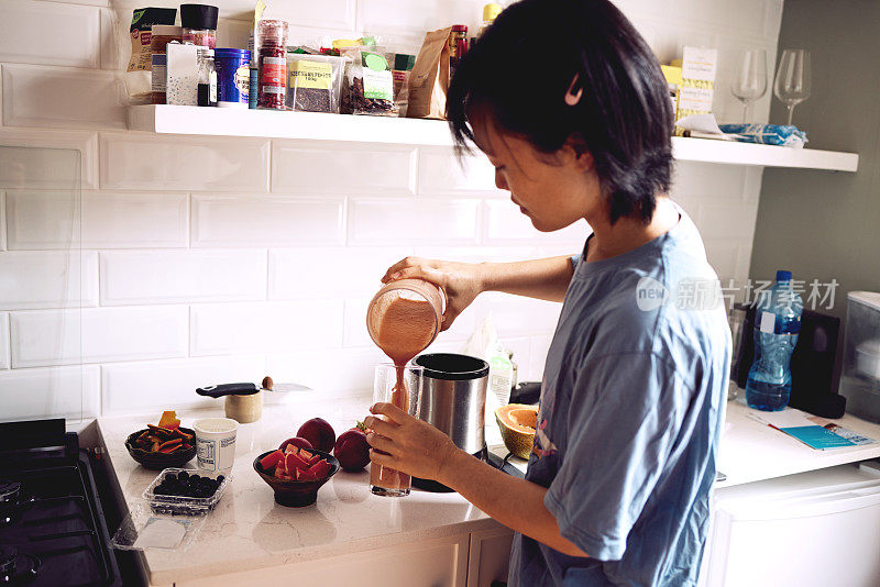 一个年轻女子在自家厨房里往杯子里倒冰沙的照片