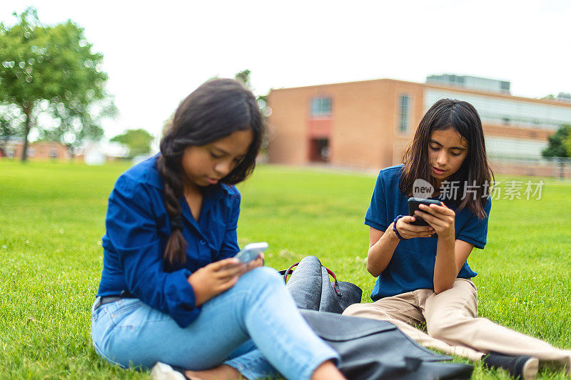 青春期前的女学生坐在校园草坪户外使用技术教育照片系列