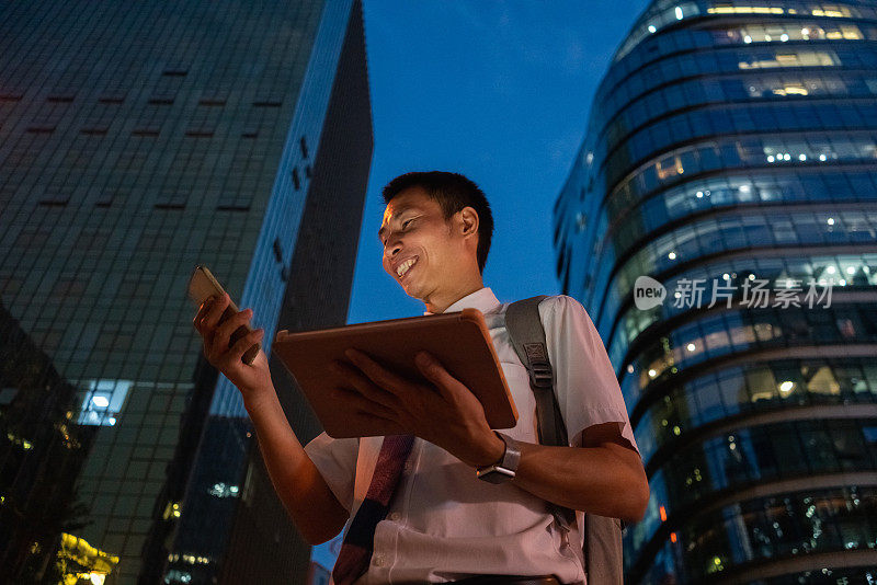 一名亚洲白领在香港中央商务区的大楼之间使用智能手机