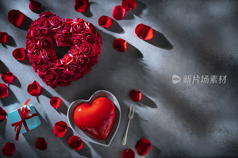 情人节的红玫瑰花瓣和心形蛋糕在灰色的复制空间