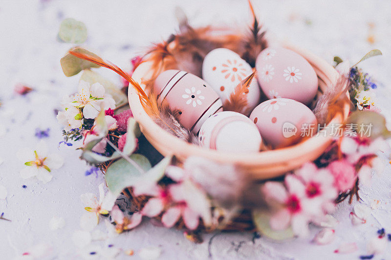 美丽的特写镜头，一个碗复活节彩蛋画在柔和的颜色和棕色的羽毛框架杏仁花和各种干花和叶子