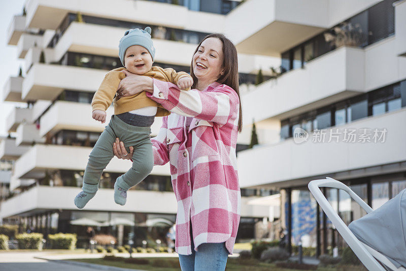 年轻的妈妈抱着婴儿，推着现代的婴儿车，漫步在城市中