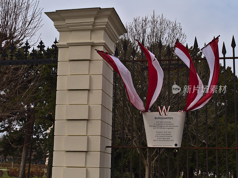 春天多云的天气里，奥地利维也纳历史中心的Burggarten公园入口处悬挂着旗帜的信息牌。