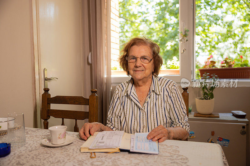 开朗的老年高加索妇女的肖像，94岁，坐在桌子和阅读一本书