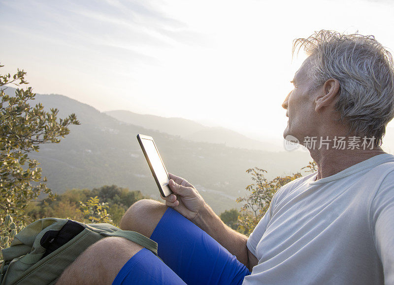 老人拿着电子阅读器在草地上休息