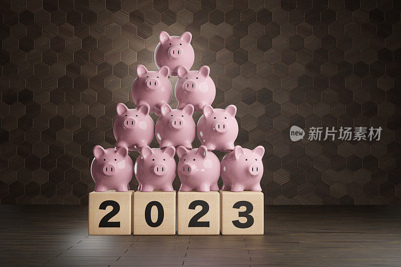 粉红色的小猪存钱罐堆放在木块上，木块上写着2023，背景是木地板和墙壁。说明2023年新的一年银行储蓄、投资和财富积累的概念