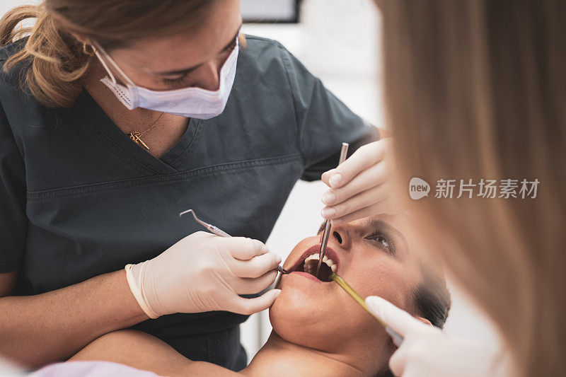 一位女牙医和她的助手在诊所检查一位病人的牙齿。卫生员使用电气设备或空气涡轮机。定期检查牙齿。