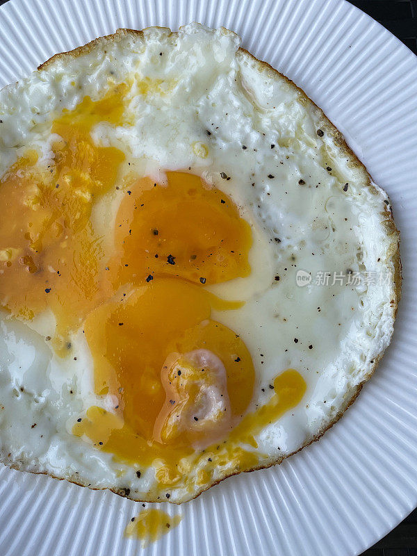全画幅画面三幅，合二为一，下熟后向阳面向上煎鸡蛋端坐在白色、棱边的盘子上，蛋黄破碎，高视