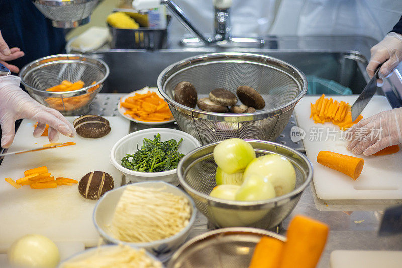 人们在厨房里切蔬菜，准备做日本学校的午餐