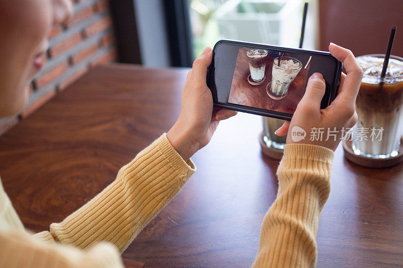 一位女士正在用智能手机给咖啡拍照。女性通过拍照在社交媒体上发布或分享受欢迎的菜肴。