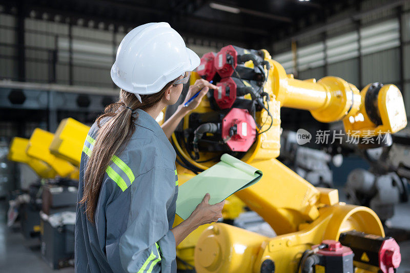 图为，在机器人仓库中，一名女工程师在给机械臂安装程序后，正在检查记录项目，并进行操作测试