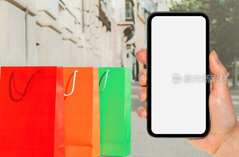 手持空白屏幕的手机，背景是五颜六色的购物袋。