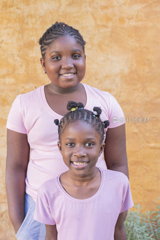 幸福的美国黑人小姐妹在户外墙背景前一起微笑的肖像