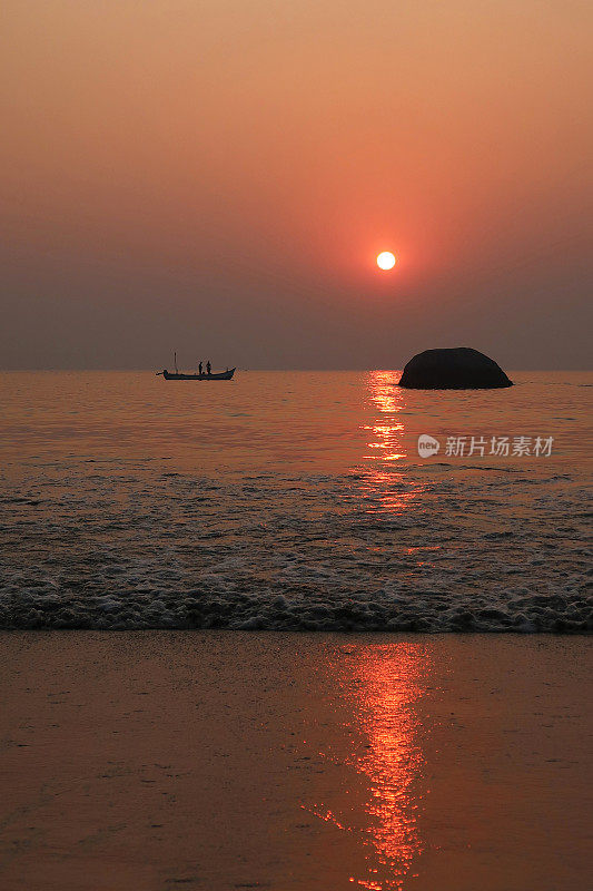 美丽的海边橙色日落日出反射在大海和潮湿的沙子，大海滩岩石在水中，渔船，潮汐反射涟漪，太阳落在海滩上的形象