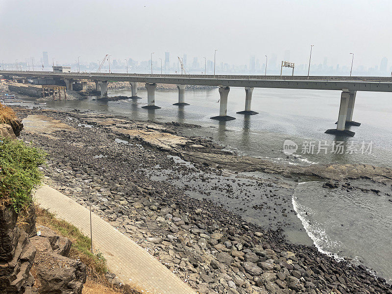 印度孟买班德拉-沃利海路(拉吉夫甘地海路)的特写图片，混凝土、斜拉桥、岩石海岸线、海水、八车道高架桥、柱子、烟雾