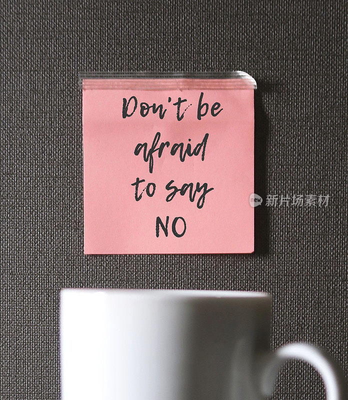 模糊的白色咖啡杯和灰色墙壁上的粉红色纸条不要害怕说不，提醒自己你是一个难以说不的人，一个寻求认可的讨人喜欢的人，一个努力让别人快乐的人