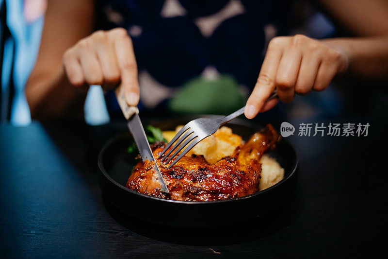一位亚洲女性在餐厅享用烤鸡腿的特写镜头
