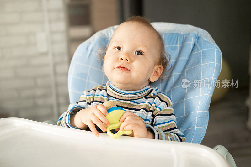 一个有趣的孩子正坐在高脚椅上，用小嚼子吃着水果。