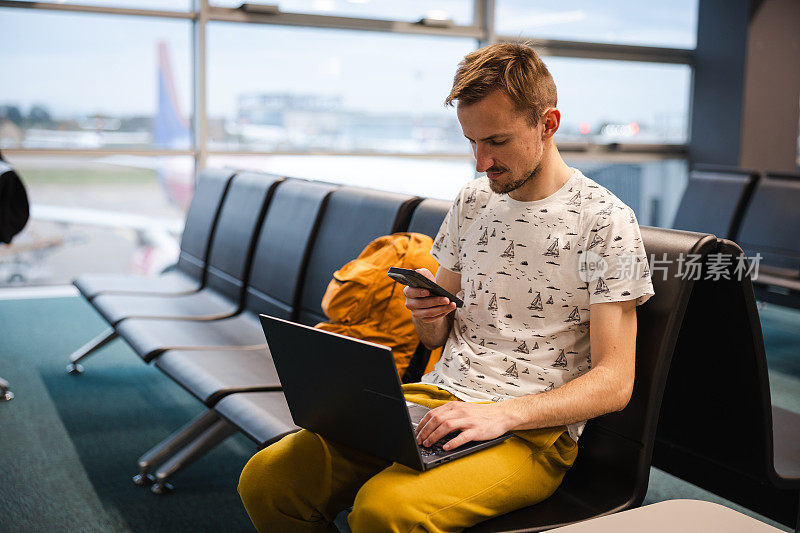 年轻的男性游客在机场候机时使用笔记本电脑