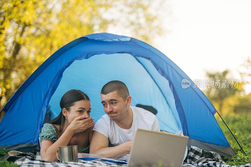 年轻的微笑情侣在帐篷里用笔记本电脑看电影。