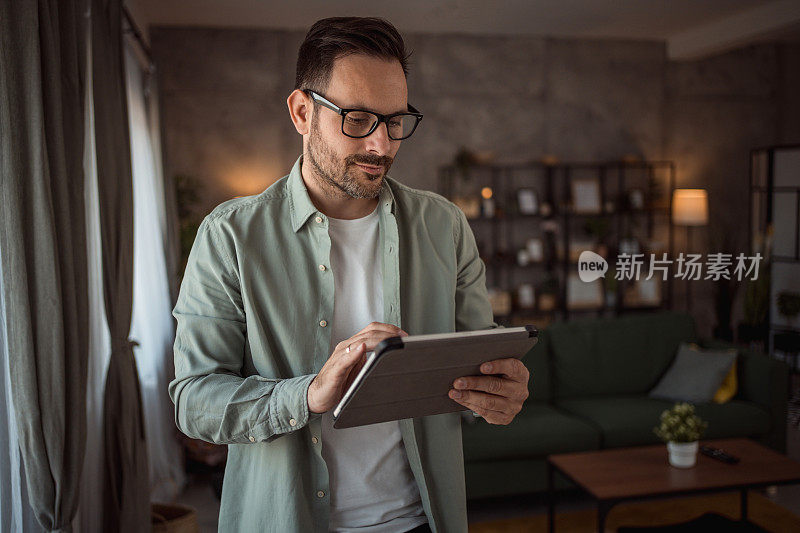 一个站在客厅窗边用平板电脑的快乐男人的画像