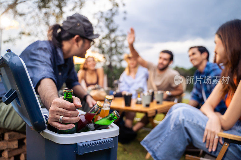 一群不同的朋友一起在帐篷里举行户外露营聚会。有魅力的年轻男女旅行者喝着酒精啤酒，享受在森林度假旅行中闲逛。