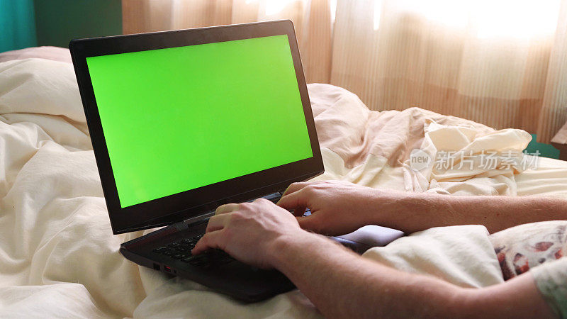 清晨，男性在床上用绿色屏幕的笔记本电脑打字