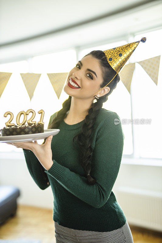 一名年轻女子在家庆祝圣诞节，手里拿着巧克力蛋糕，蛋糕上插着2021年的蜡烛