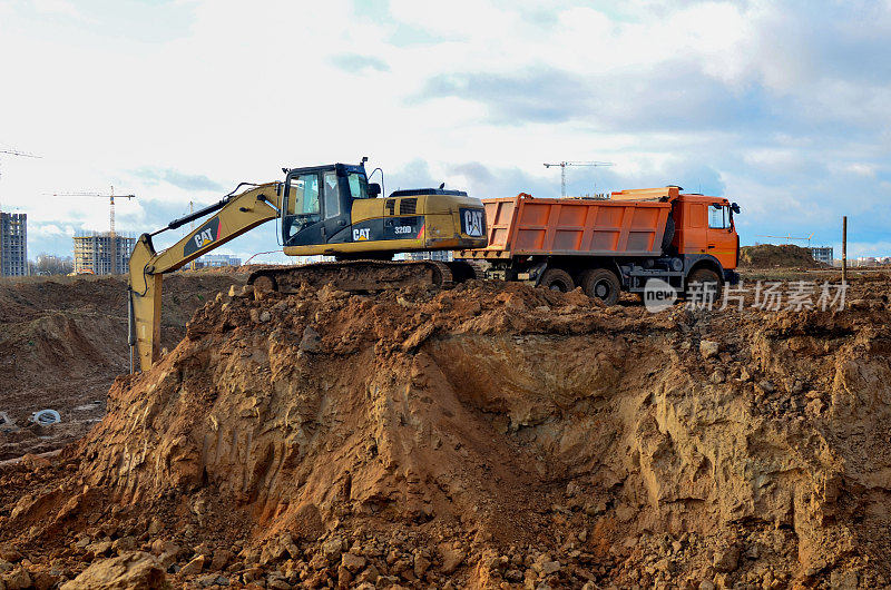 挖掘机卡特彼勒320L在施工现场将沙子装载到重型自卸车MAZ上
